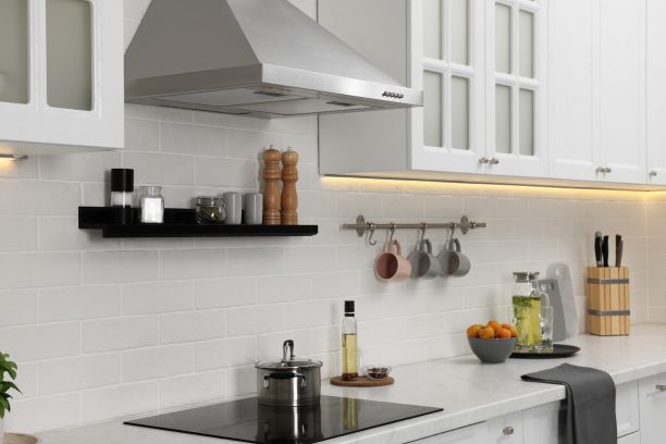 a tile backsplash with a hood fan and white cabinets